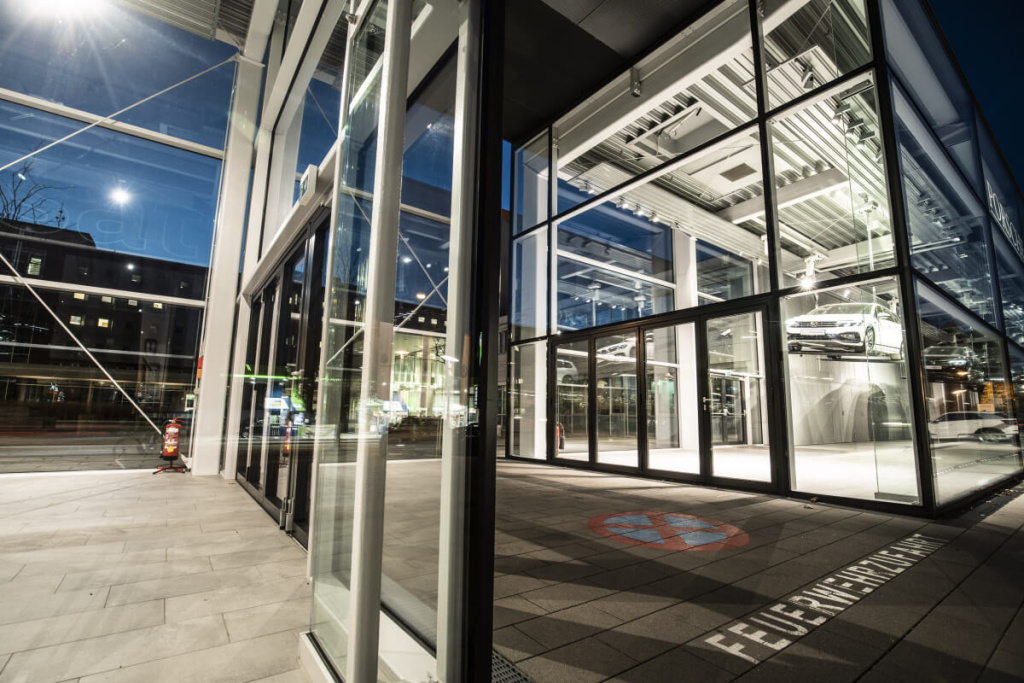Glasfassade des Porsche-Showrooms bei Nacht mit Parkplatzmarkierung.