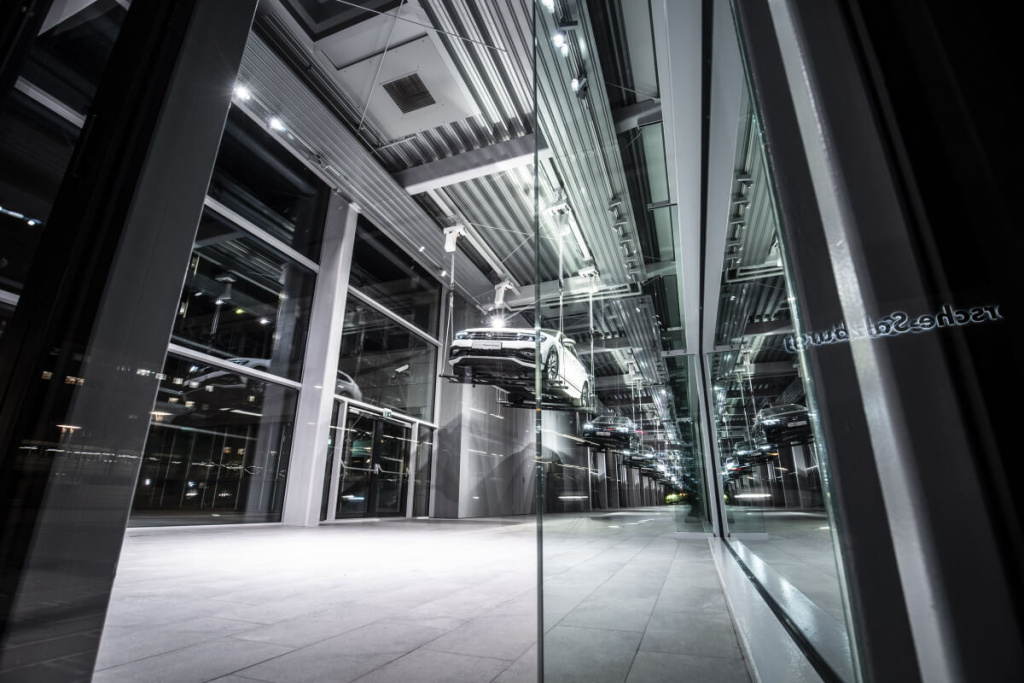 Moderne Architektur des Porsche-Zentrums mit reflektierendem Glas und schwebendem Fahrzeug.
