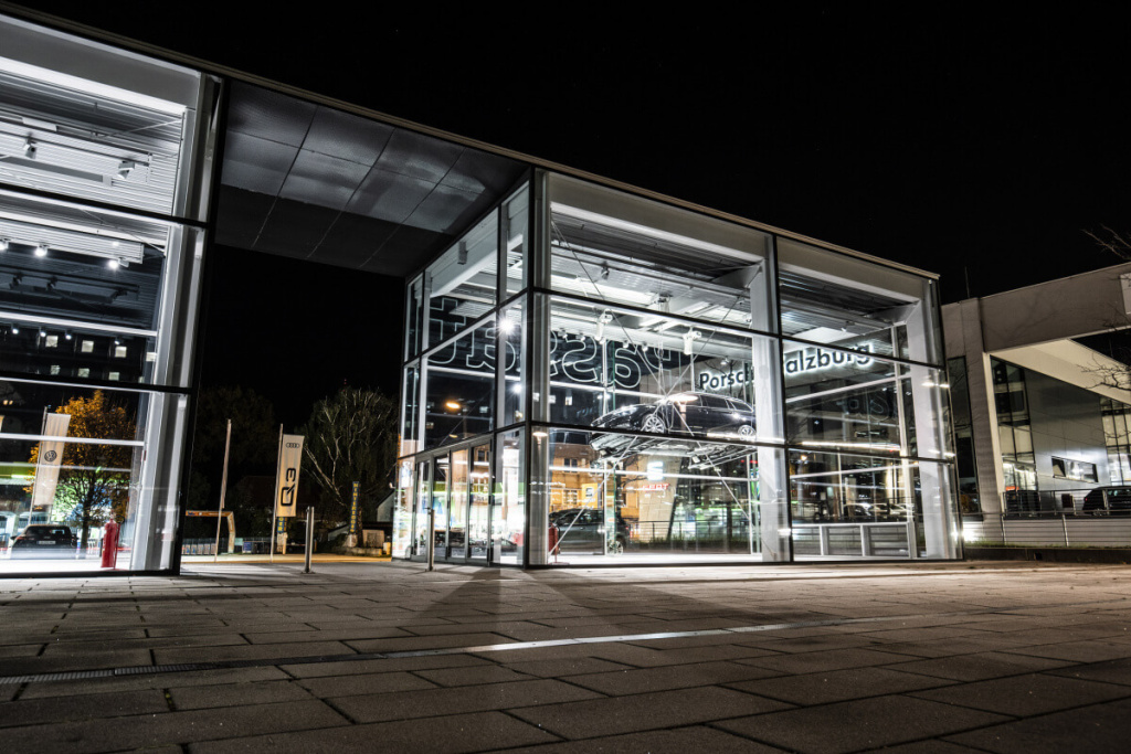 Moderne Porsche-Niederlassung in Salzburg bei Nacht, mit klaren Glasfronten und Beleuchtung.