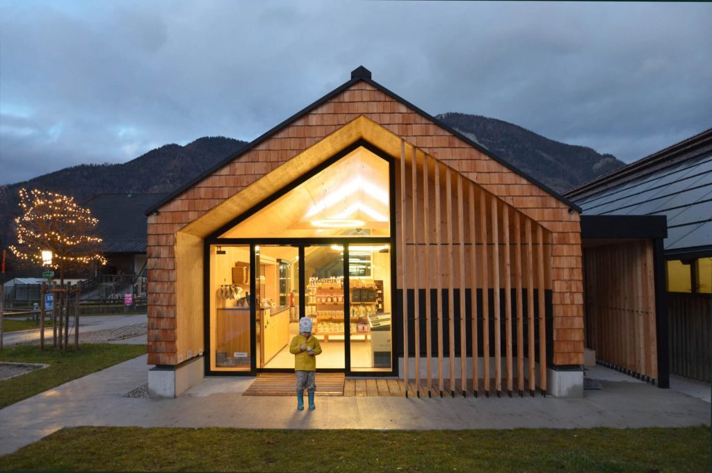 Holzarchitektur des Selbstbedienungs-Hofladens WOLKE7 in der Abenddämmerung.