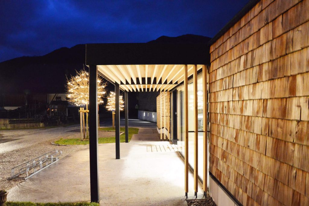 Moderne Architektur des Selbstbedienungs-Hofladens WOLKE7 bei Nacht, Holzfassade und Beleuchtung.